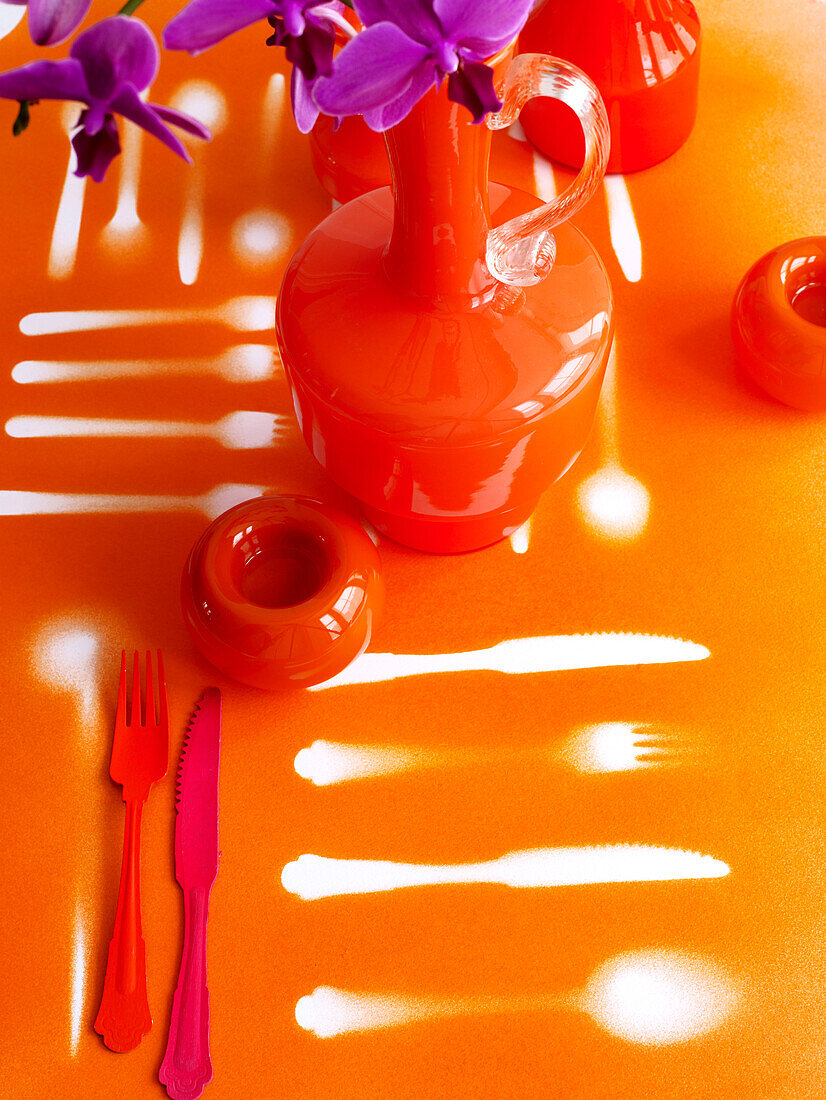 Orangefarbene Gläser und Bestecke mit Umrissen in Sprühfarbe auf der Tischplatte