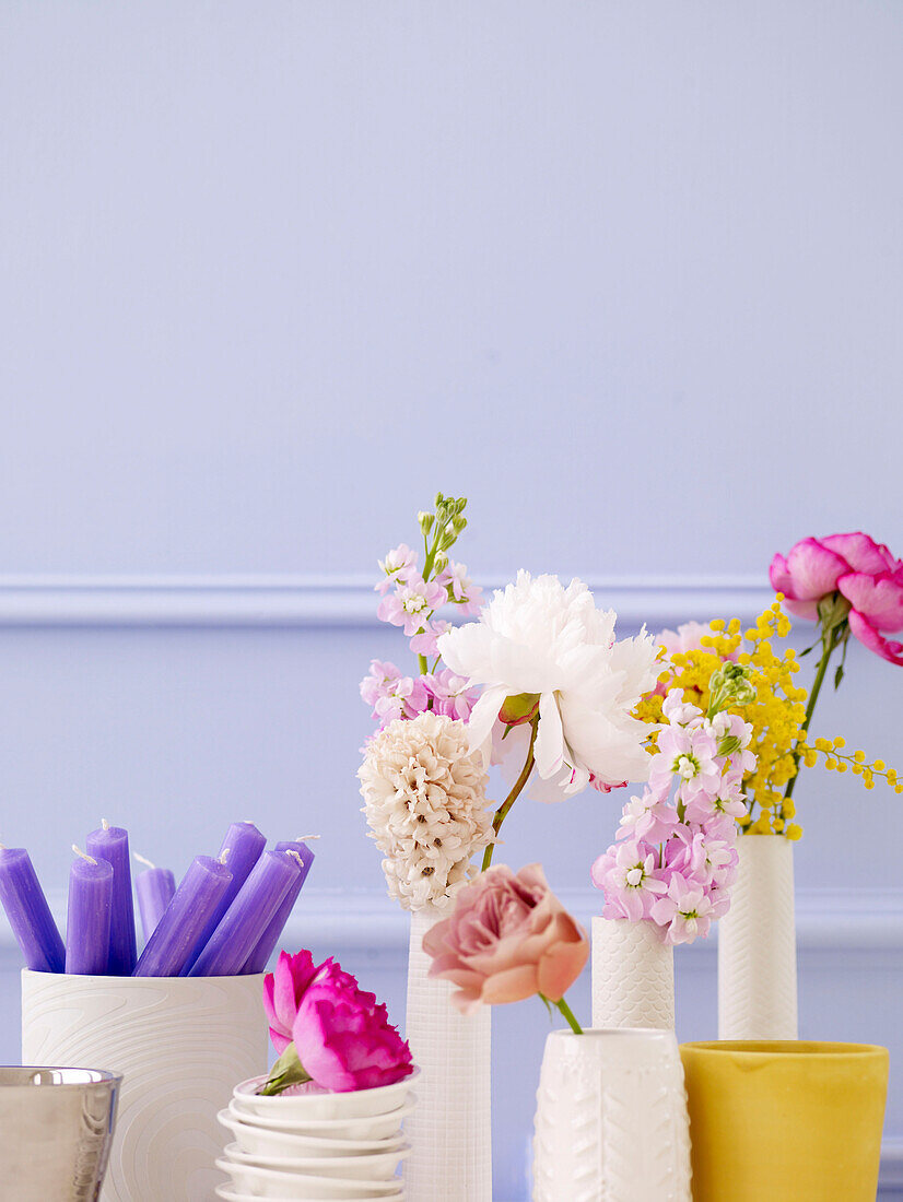 Einblütige Blumen und violette Kerzen in weißen Keramikvasen