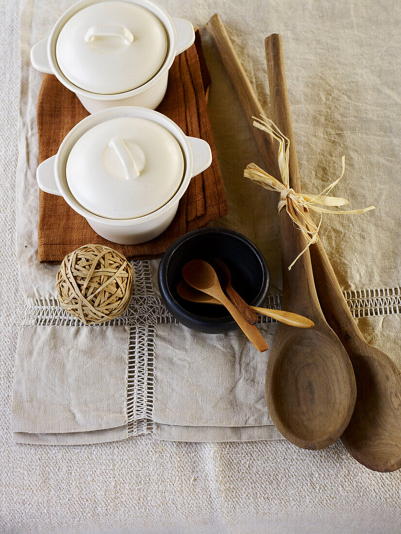 Holzlöffel und Keramiktöpfe mit elastischem Kugelband auf Leinentischsets