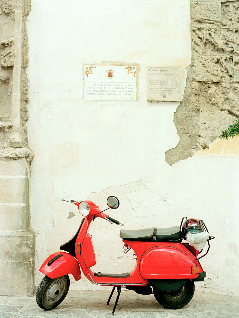 Leuchtend roter Motorroller vor einer weiß gewaschenen Fassade geparkt Spanien