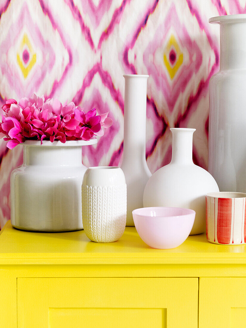 Collection of white ceramic vases on yellow sideboard with geometric patterned wallpaper