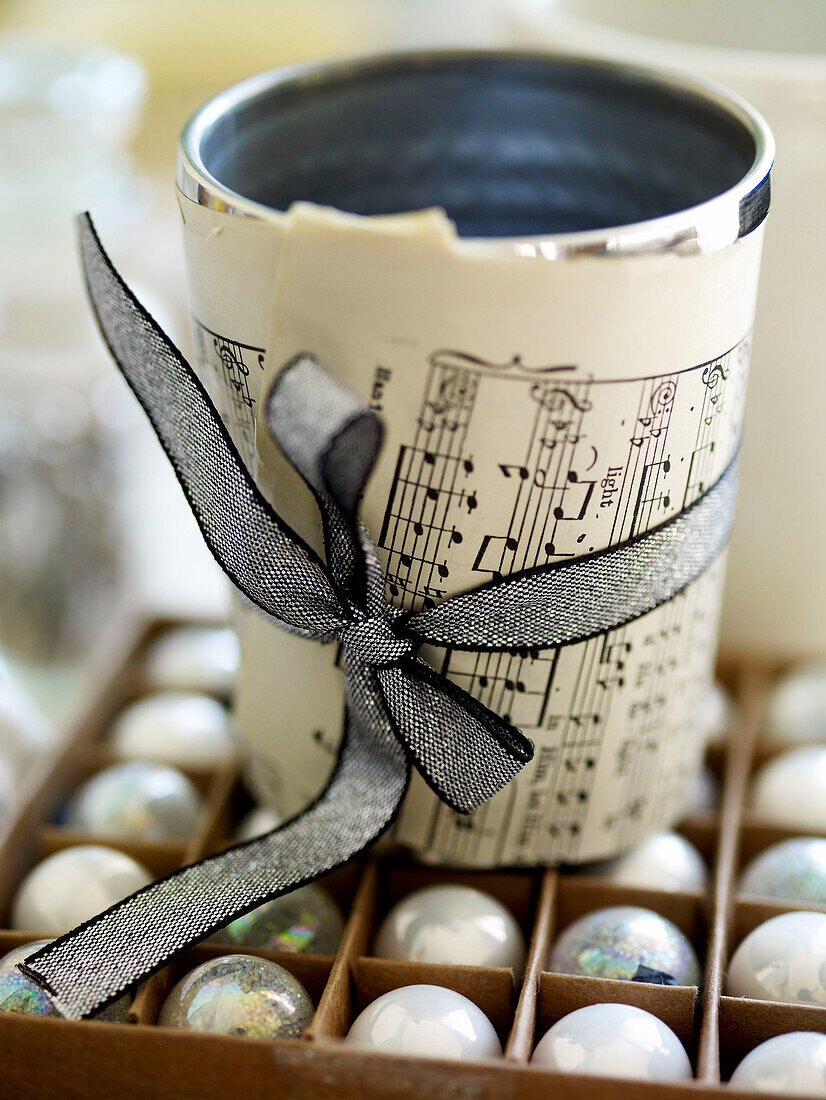 Tin cup wrapped with sheet music tied with ribbon on box of baubles