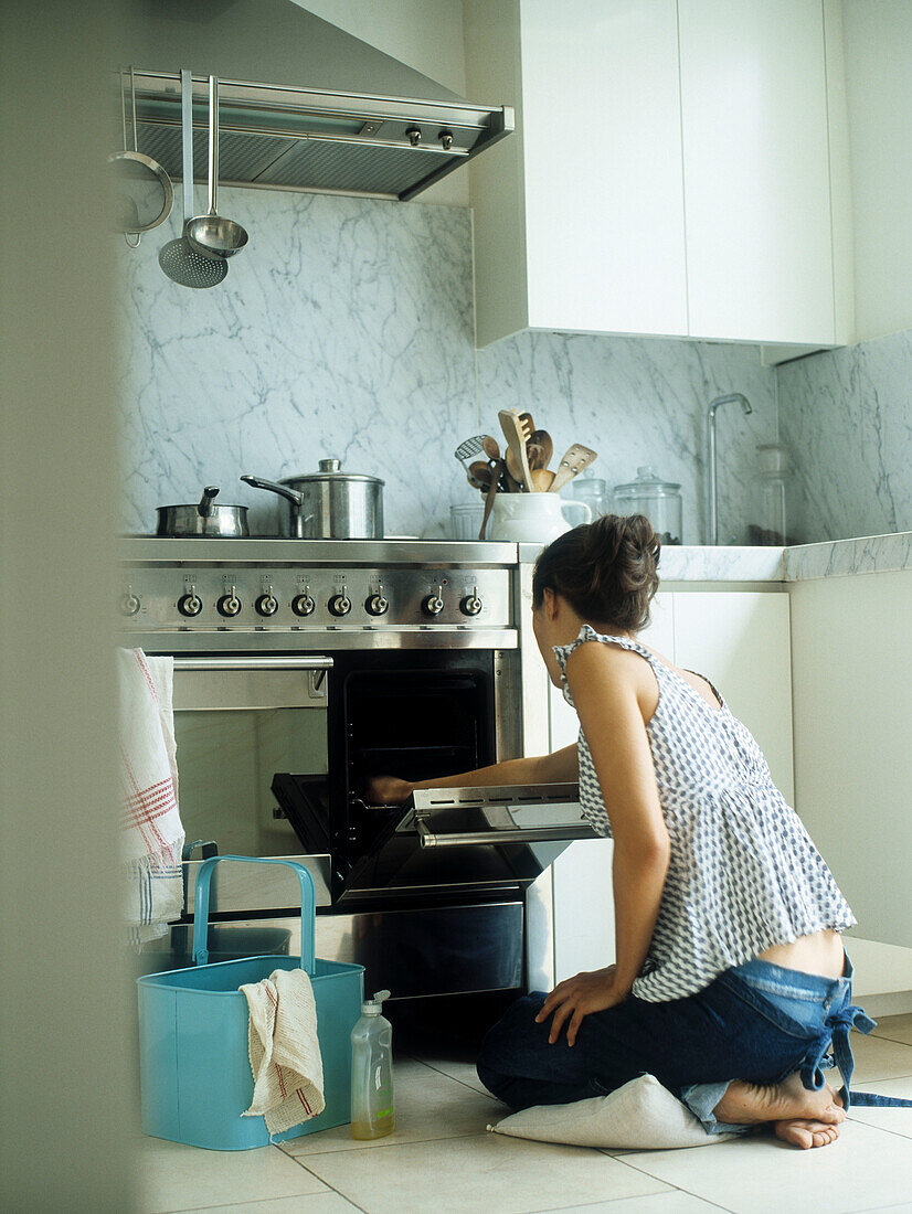 Frau kniet auf einem Kissen, während sie den Ofen reinigt