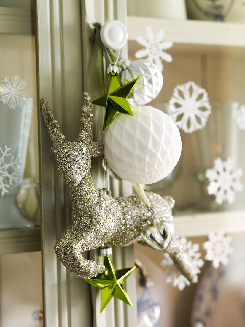 Glitzerndes Rentier und Weihnachtskugel mit Sternen auf Glasvitrine mit Schneeflocken