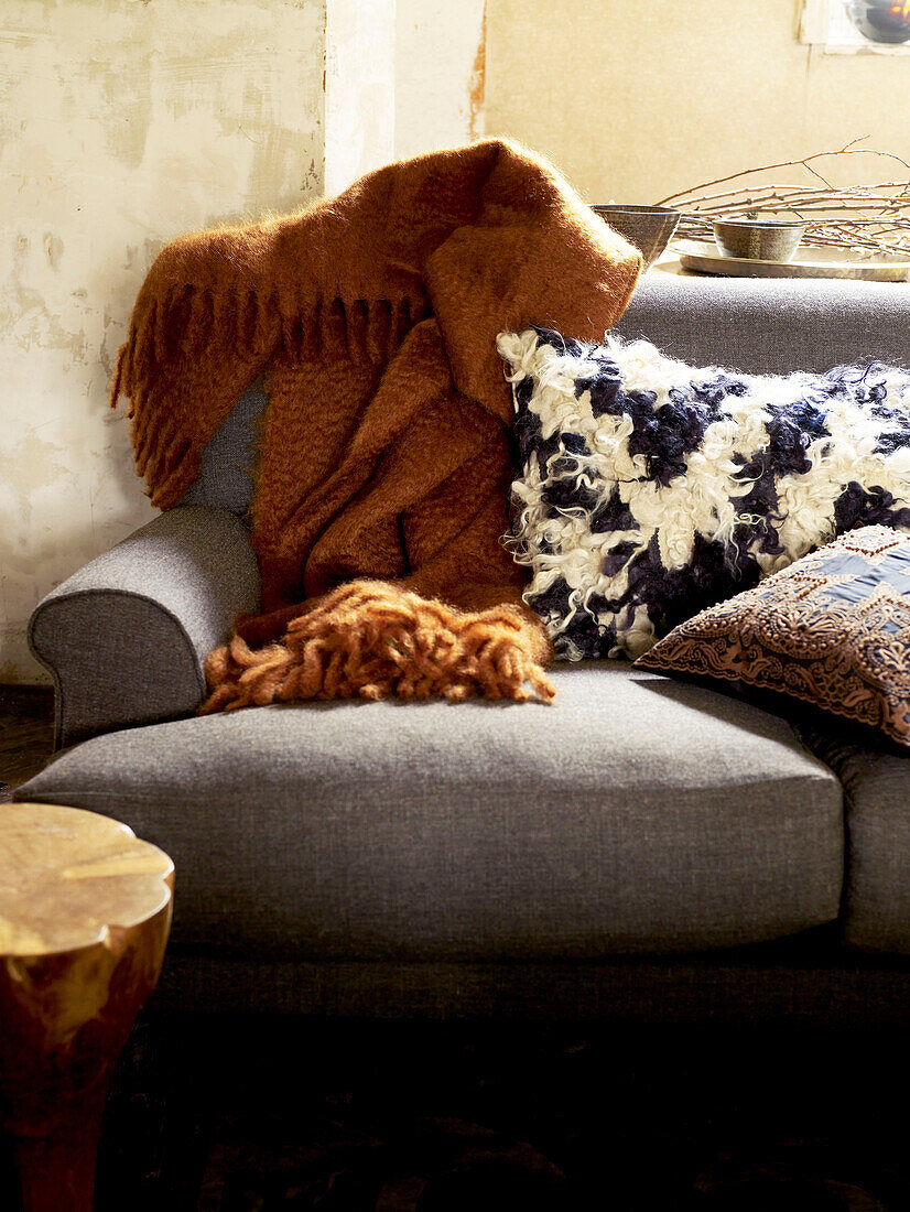 Wolldecke und Kissen auf sonnenbeschienenem grauem Sofa