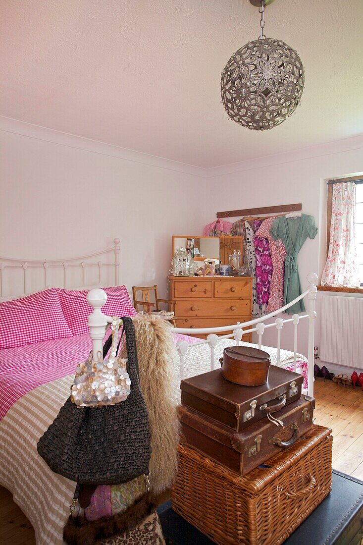 Braune Lederkoffer im Schlafzimmer mit verschnörkelter Metallpendelleuchte in einem Haus in Cranbrook, Kent, England, UK