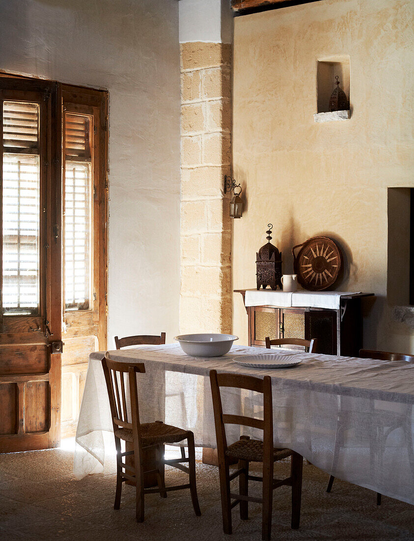 Holzstühle am Tisch mit weißem Tuch im sonnenbeschienenen Eingangsbereich eines traditionellen sizilianischen Hauses