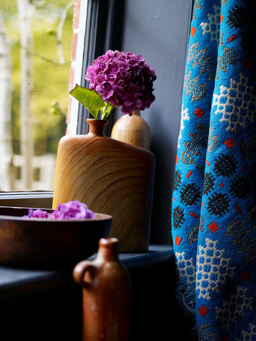 Bunte Hortensien in Holzvase auf Fensterbank mit blauem Vorhangstoff