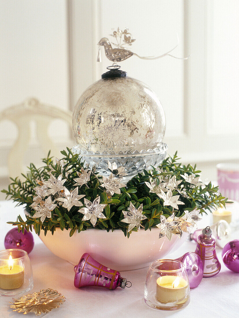Glaskugel und Blumen mit rosa Glöckchen und brennenden Teelichtern
