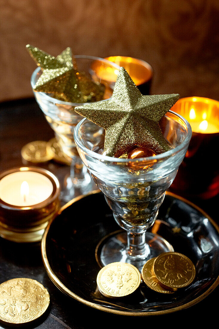 Goldsterne in Weingläsern mit brennenden Teelichtern und Münzen