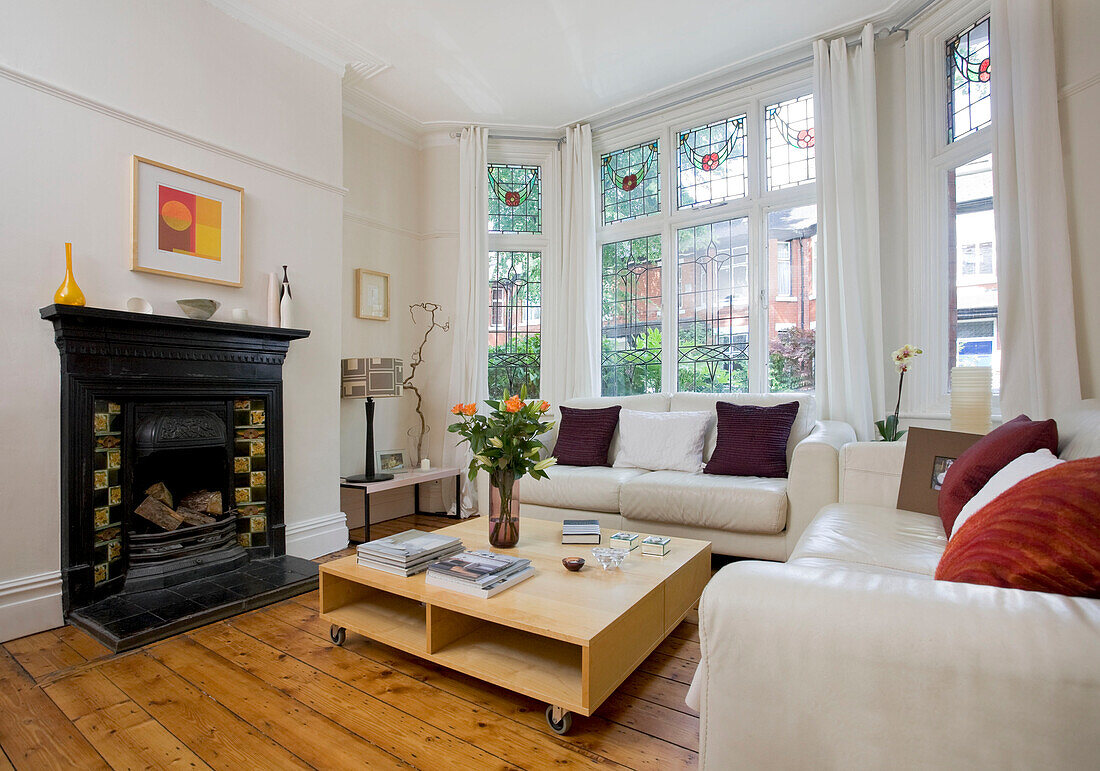 Victorian fireplace and low coffee table with white leather sofas in Manchester family home, England, UK