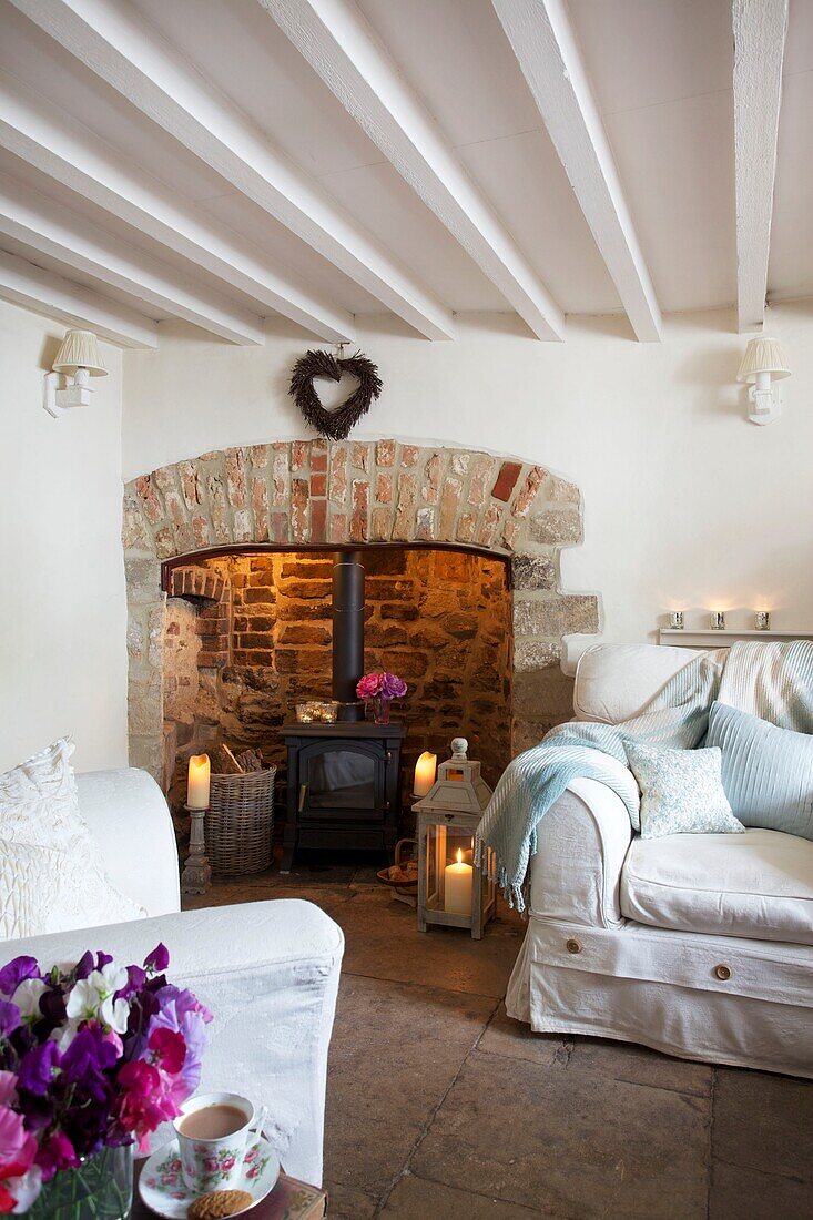 Exposed brick fireplace and white painted beamed ceiling with slip cover upholstering in living room of Corfe Castle cottage, Dorset, England, UK