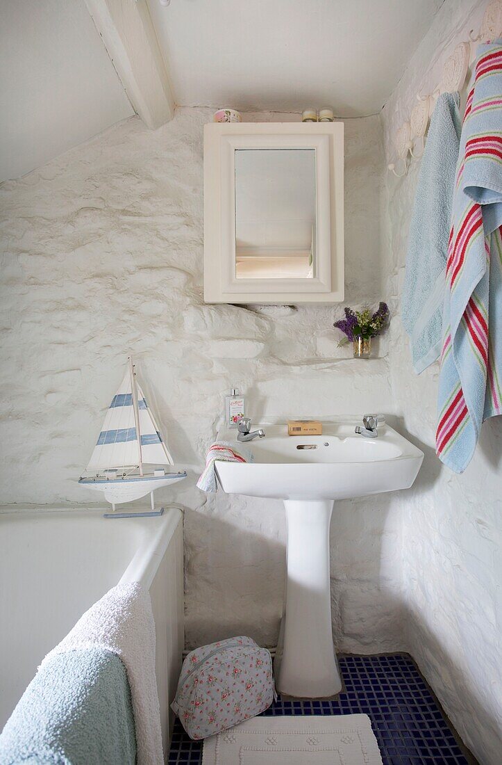 Standwaschbecken und Wandschrank im weiß getünchten Badezimmer eines Cottages in Corfe Castle, Dorset, England, UK
