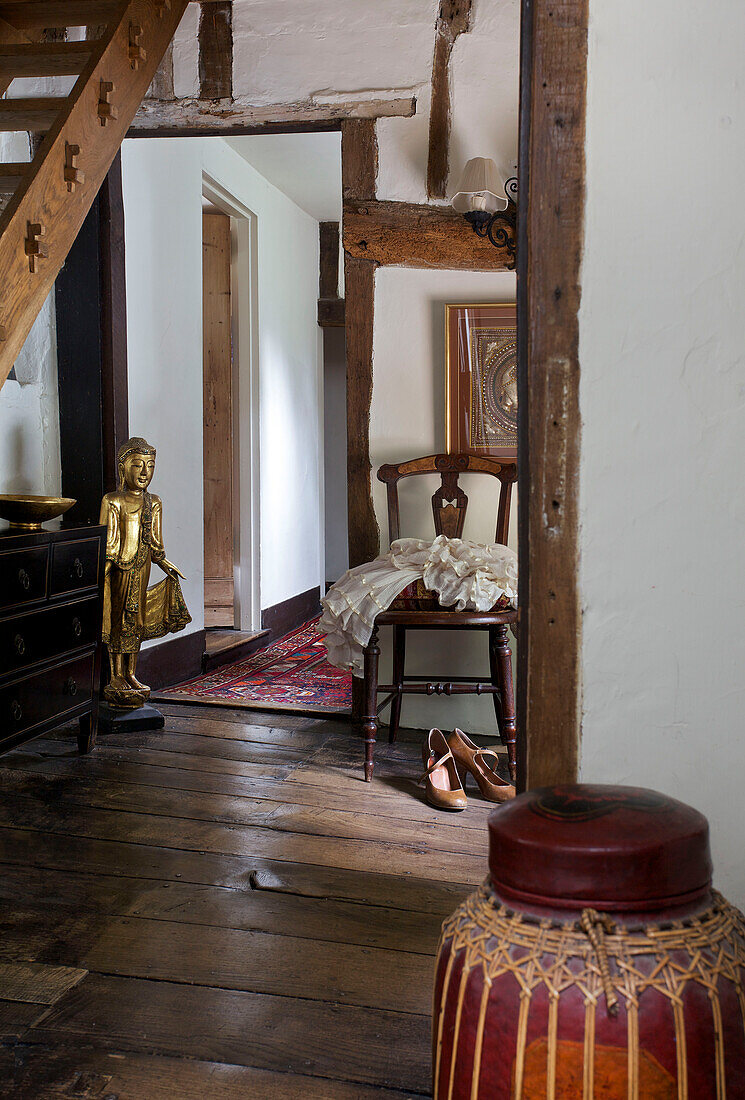 View through doorway to hallway with buddha statue and chair with shoes in Sandhurst cottage, Kent, England, UK