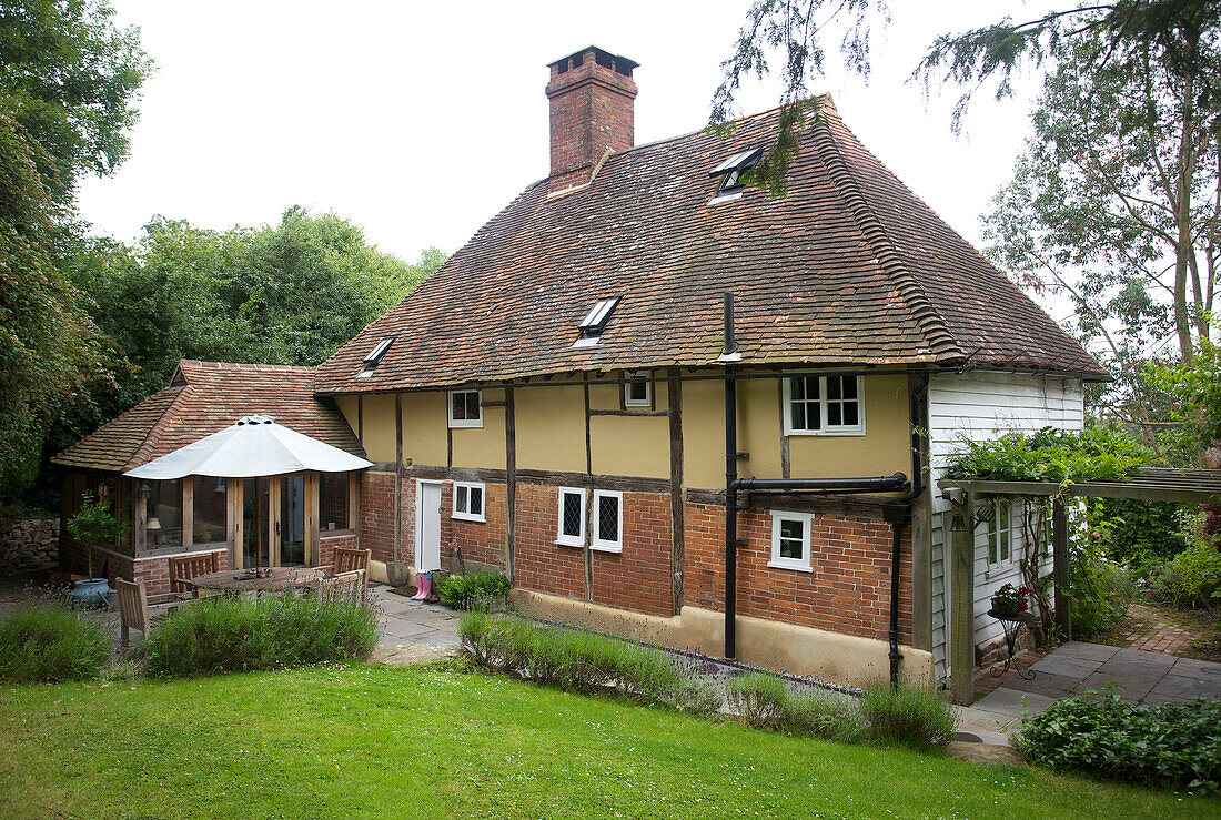 Sonnenschirm, Tisch und Stühle in einem Garten mit Rasen vor einem Fachwerkhaus in Sandhurst, Kent, England, UK