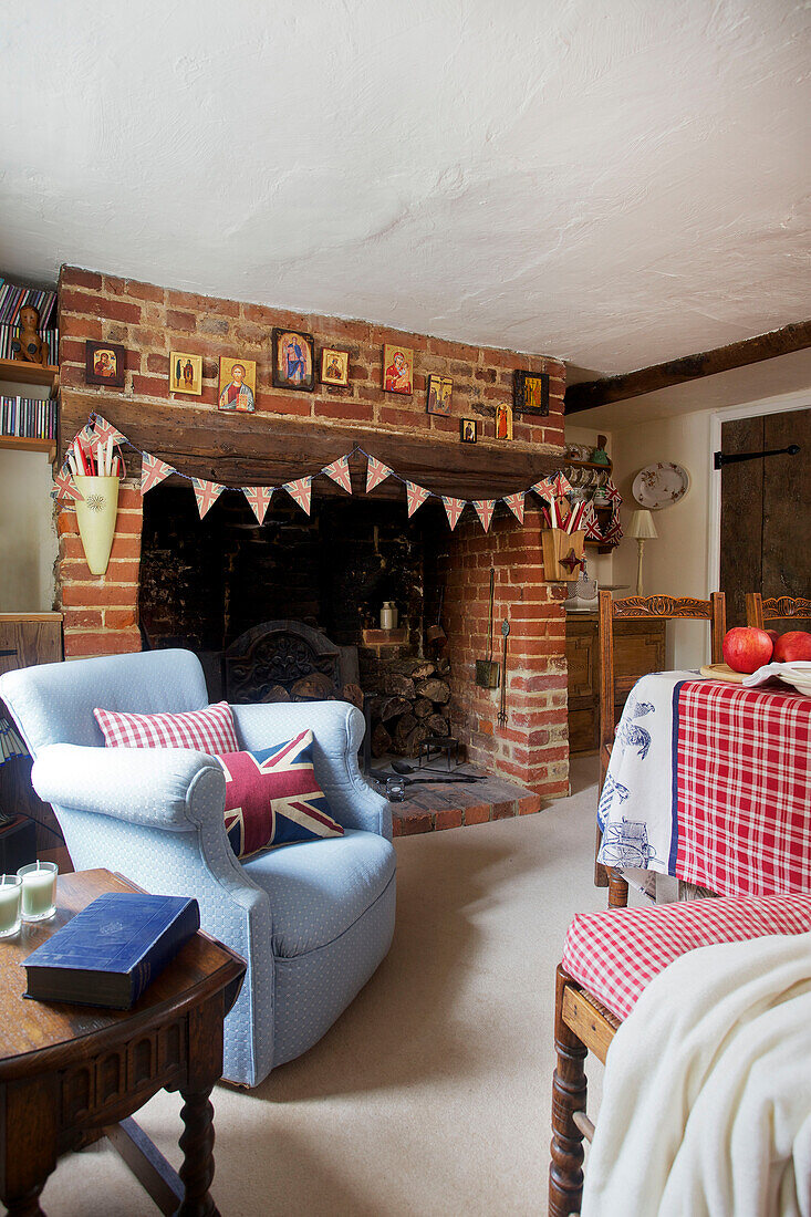 Light blue armchair by fireplace with bunting in Egerton cottage, Kent, England, UK