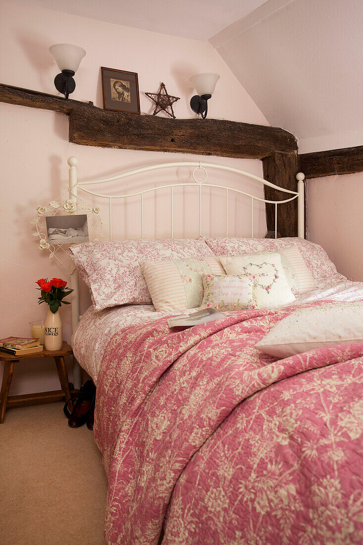 Pink floral patterned bed covers in attic bedroom of Egerton cottage, Kent, England, UK