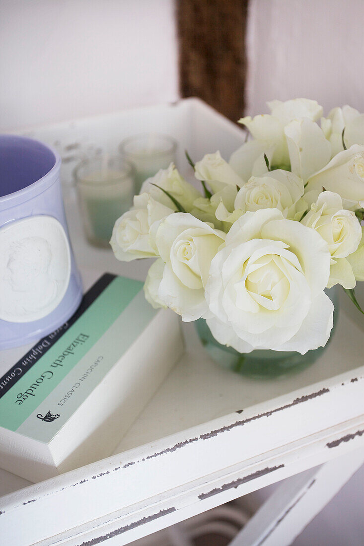 Freshly cut white roses and book on bedside table in Egerton cottage, Kent, England, UK