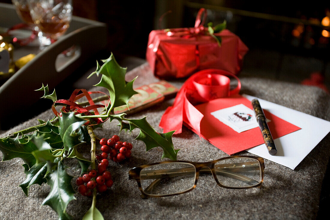 Stechpalmenzweig mit Lesebrille und Weihnachtsumschlägen in einem Haus in Tenterden, Kent, England, UK