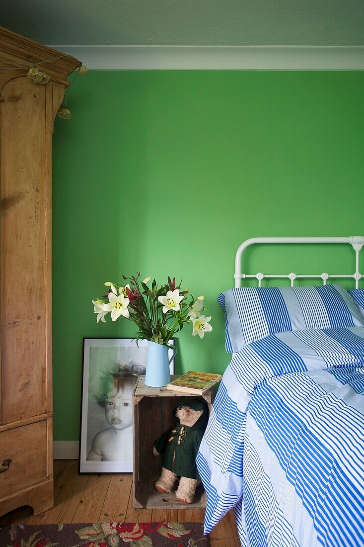 Cut lilies on wooden bedside crate in bright green bedroom of Cranbrook family home, Kent, England, UK