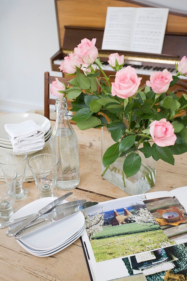 Geschnittene Rosen und Glaswaren auf einem Tisch mit Quellenbuch und Klavier in einem Haus der Familie in Tenterden, Kent, England, UK