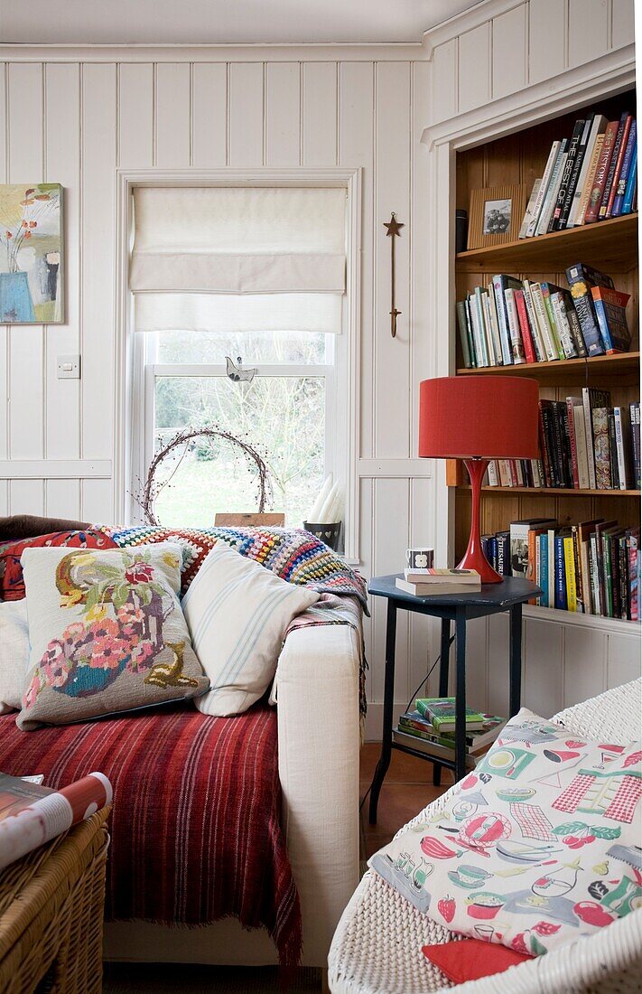 Cushions on sofa at window with bookcase, in Tenterden family home, Kent, England, UK