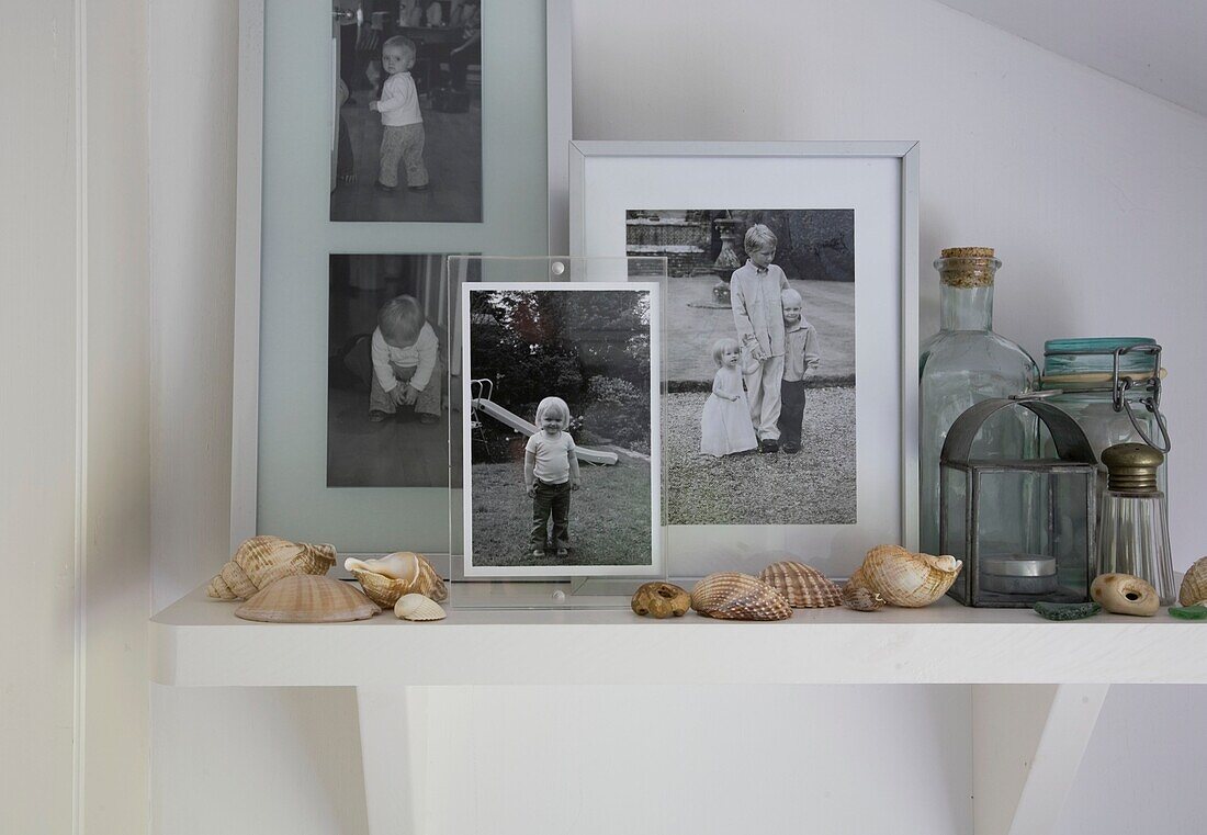 Black and white family photographs with seashells and antique glassware on shelf in Tenterden artist's home, Kent, England, UK