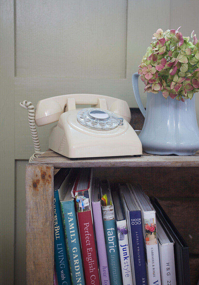 Cremefarbenes Wählscheibentelefon mit Hortensien auf einem hölzernen Bücherregal in einem Bauernhaus in High Halden, Kent, England, UK