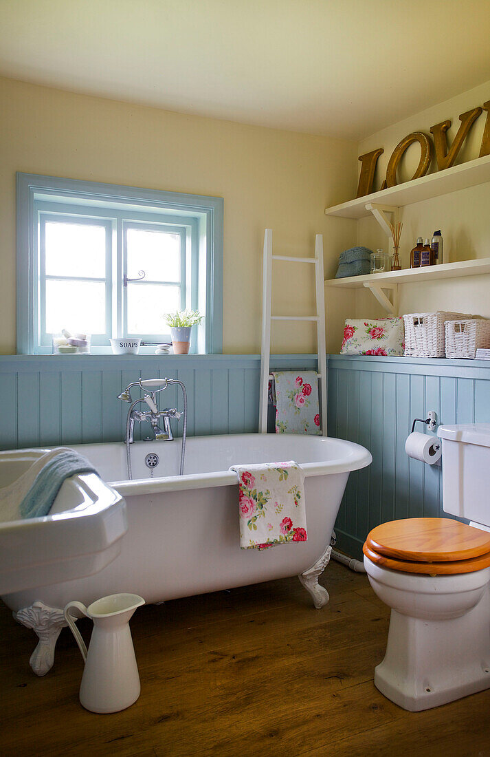 Freistehende Badewanne aus weißer Keramik in einem blau getäfelten Badezimmer in einem Bauernhaus in High Halden, Kent, England, Vereinigtes Königreich