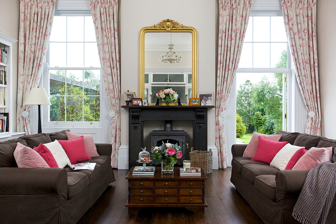 Gilt framed mirror on mantlepiece with pink cushions on sofas living room of Kilndown home Cranbrook Kent England UK