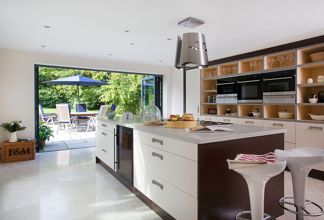 Kitchen island with view through open doors to terrace seating in modern home Bath Somerset, England, UK