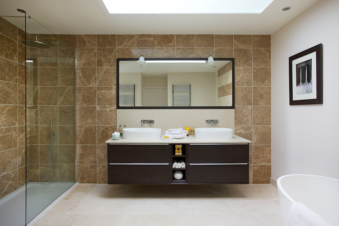 Doppelwaschbecken in einem braun gefliesten Badezimmer mit Glasduschkabine in einem modernen Haus in Bath Somerset, England, UK