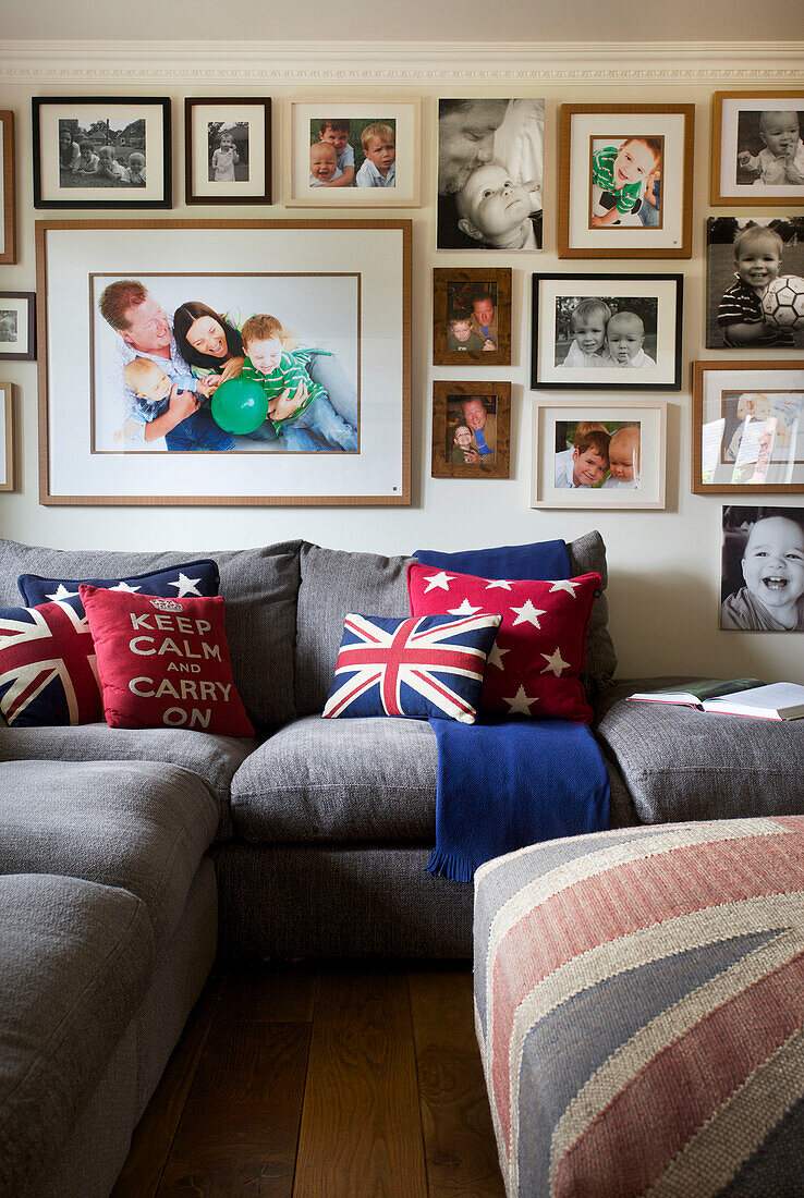 Familienfotos an der Wohnzimmerwand über einem grauen Sofa mit Union-Jack-Kissen in einem Haus in Smarden, Kent, Großbritannien