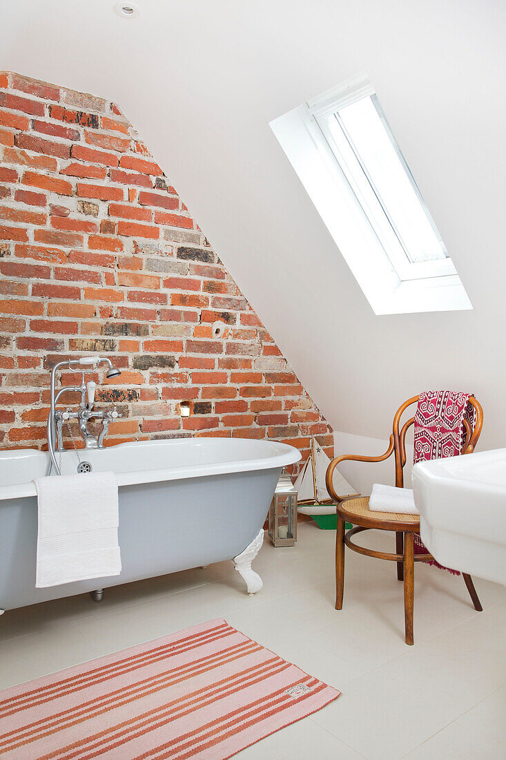 Freigelegte Ziegelwand mit freistehender Badewanne im Dachgeschoss-Badezimmer eines Strandhauses in Emsworth, Hampshire, England, UK