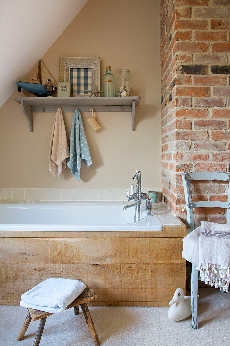 Painted chair with wood panelled bath in exposed brick bathroom of Kent farmhouse England UK