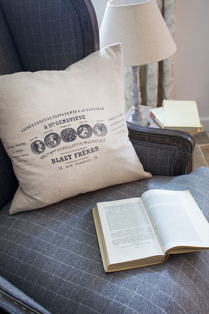 Cream cushion and book on grey upholstered armchair in Dorset cottage Corfe Castle England UK