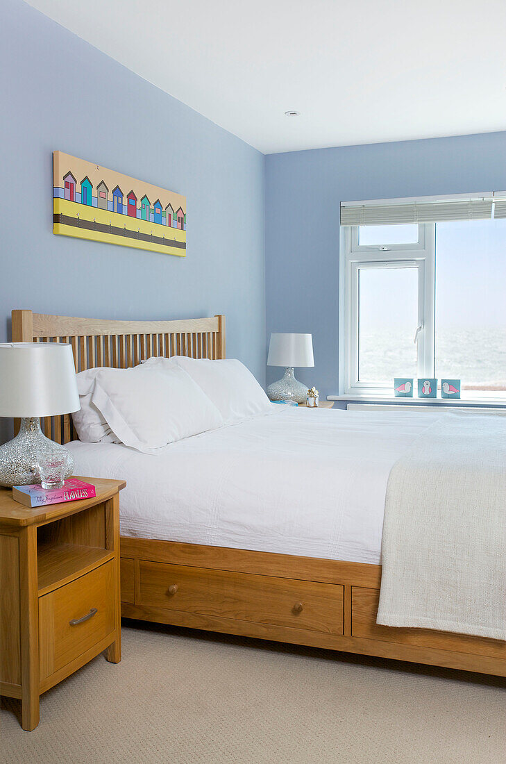 Weiße Bettdecke und Kissen auf einem Doppelbett im blauen Schlafzimmer eines Strandhauses auf Hayling Island, Hampshire, England, UK