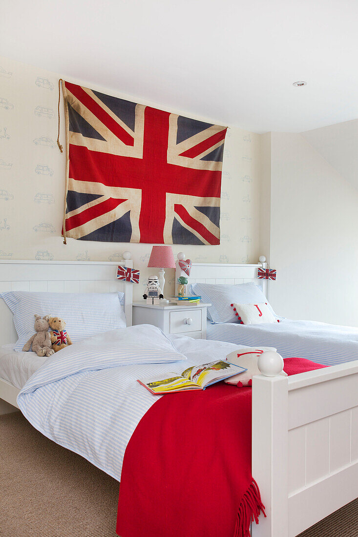 Union Jack hängt über Doppelbetten mit blau gestreiften Bettdecken und roter Decke in einem Haus in Kilndown, Cranbrook, Kent, England, UK