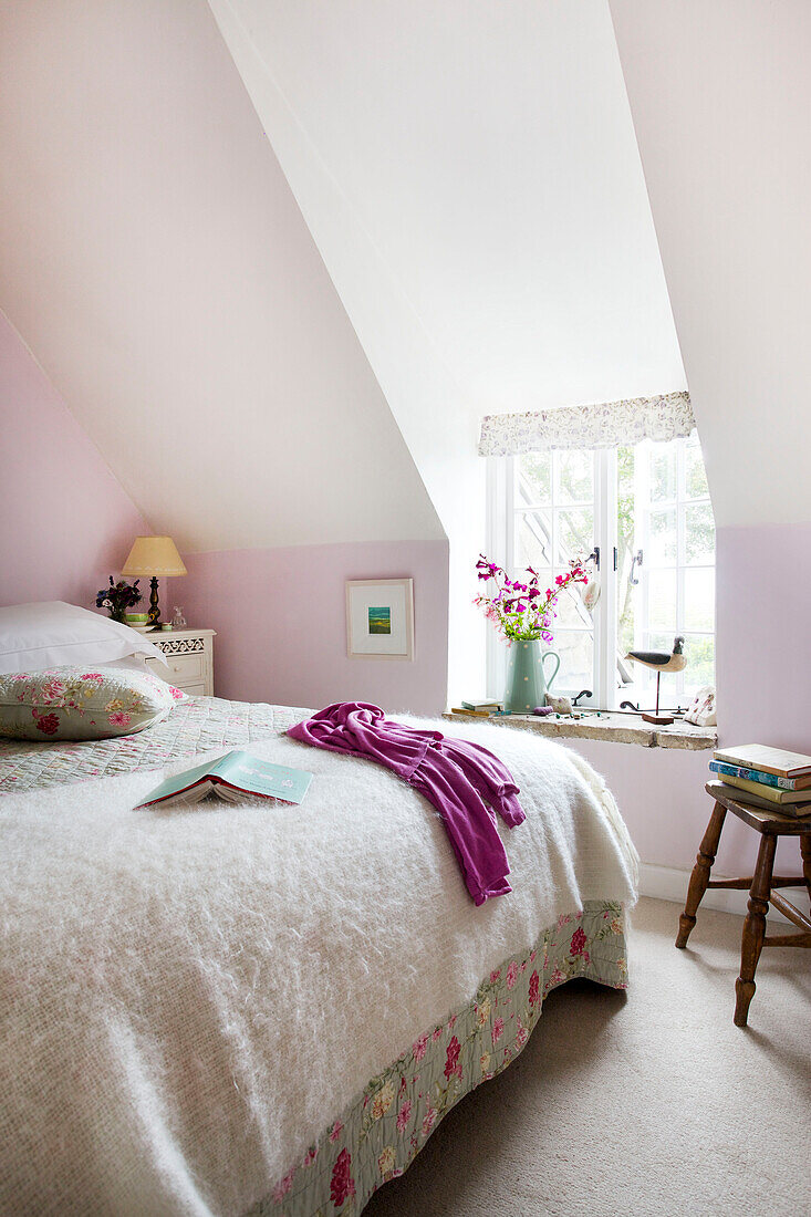 Pink cardigan and book on double bed with dormer window in Worth Matravers cottage Dorset England UK