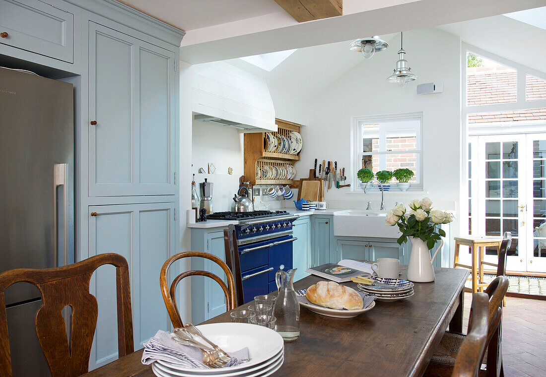 Brot und geschnittene Rosen auf Holztisch in hellblauer Küche eines Hauses in Emsworth, Hampshire, England, UK