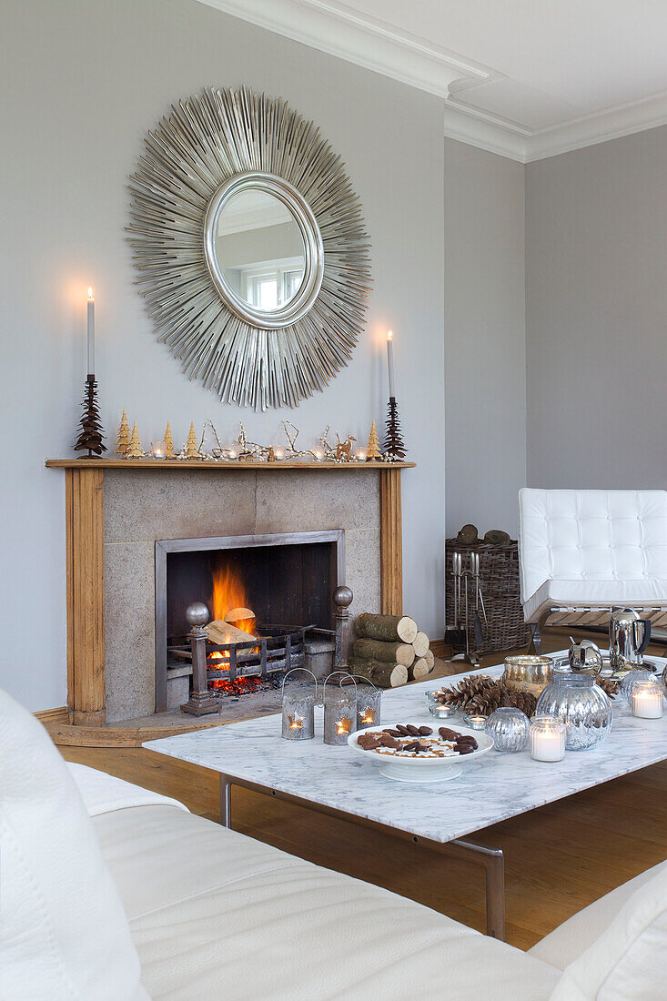 Circular mirror above lit fire in white living room of Faversham home Kent England UK