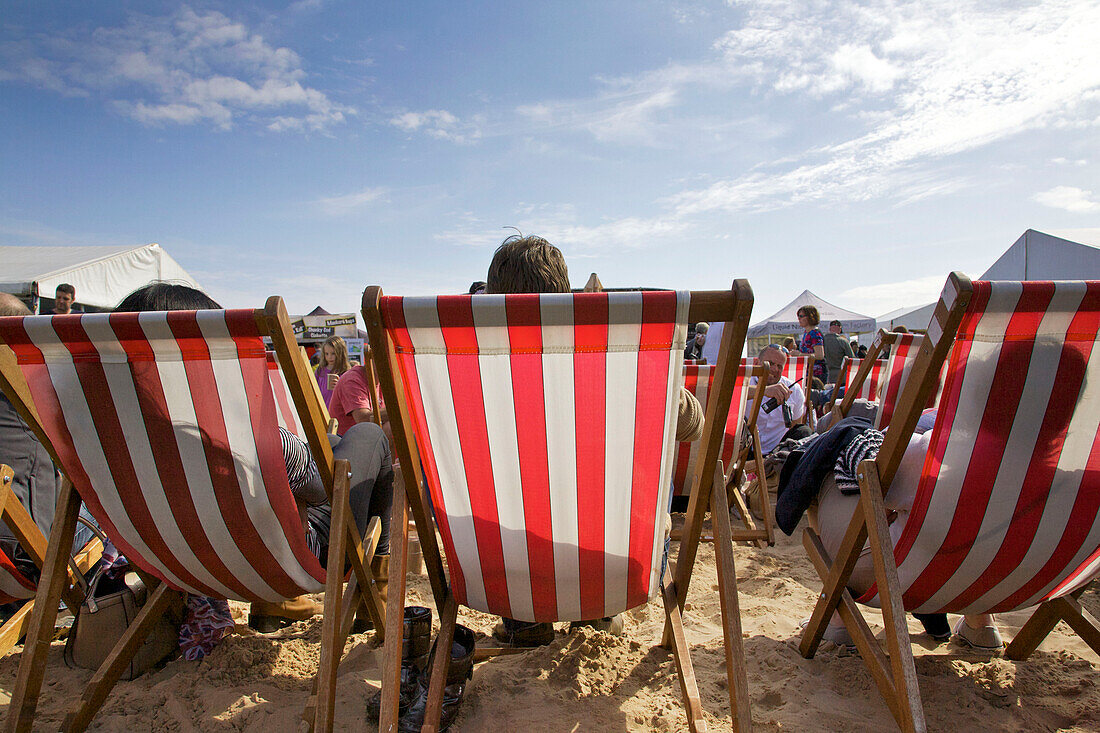 Menschen sitzen auf rot gestreiften Liegestühlen am Strand von Brighton Sussex England UK