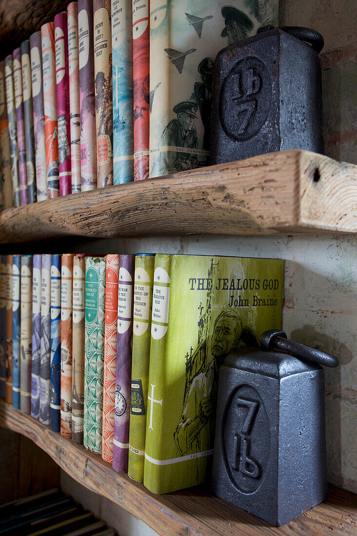 Vintage books with antique weights on salvaged shelves in Grade ll listed windmill conversion Kent UK