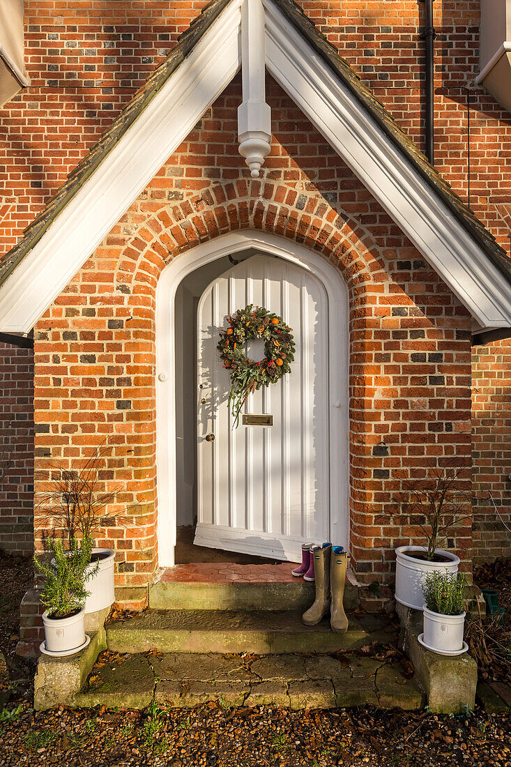 Stiefel auf der Türschwelle mit Weihnachtskranz an der Vordertür des 1829 erbauten Pfarrhauses in Warehorne, Kent, UK