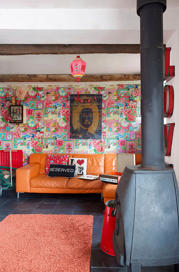 Orangefarbenes Ledersofa mit gemusterter Vintage-Tapete in einem Wohnzimmer in Tenterden, Kent, Großbritannien