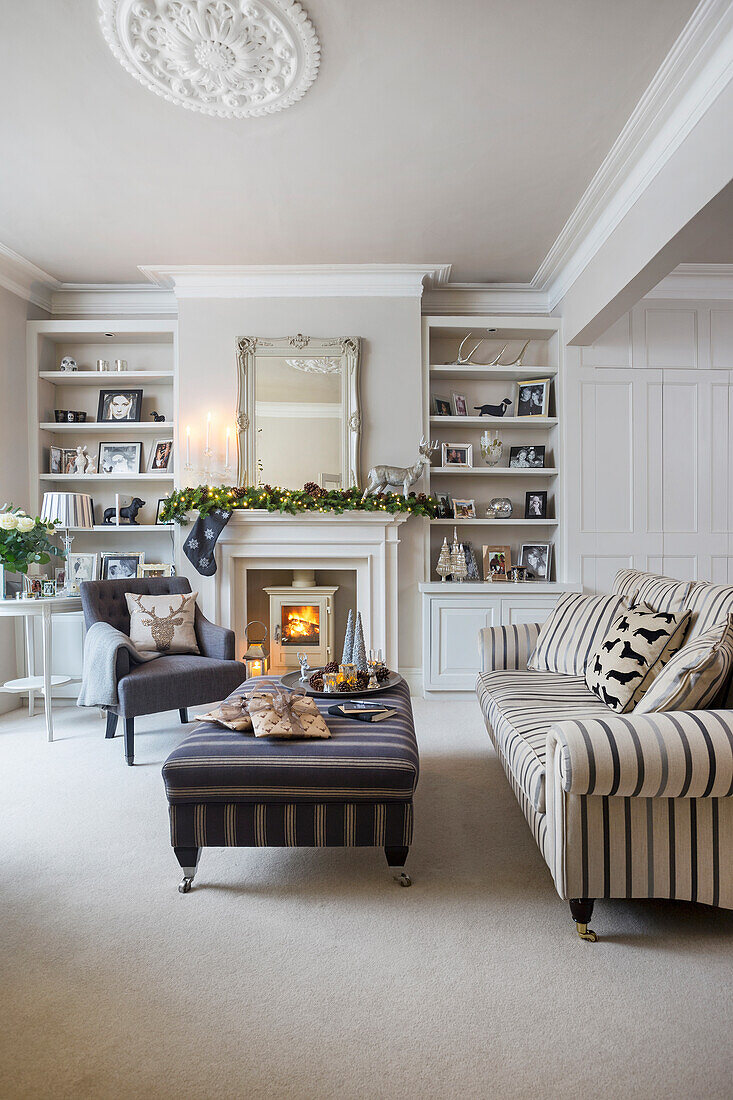 Striped sofa and ottoman with lit woodburner and Christmas decorations in London home UK