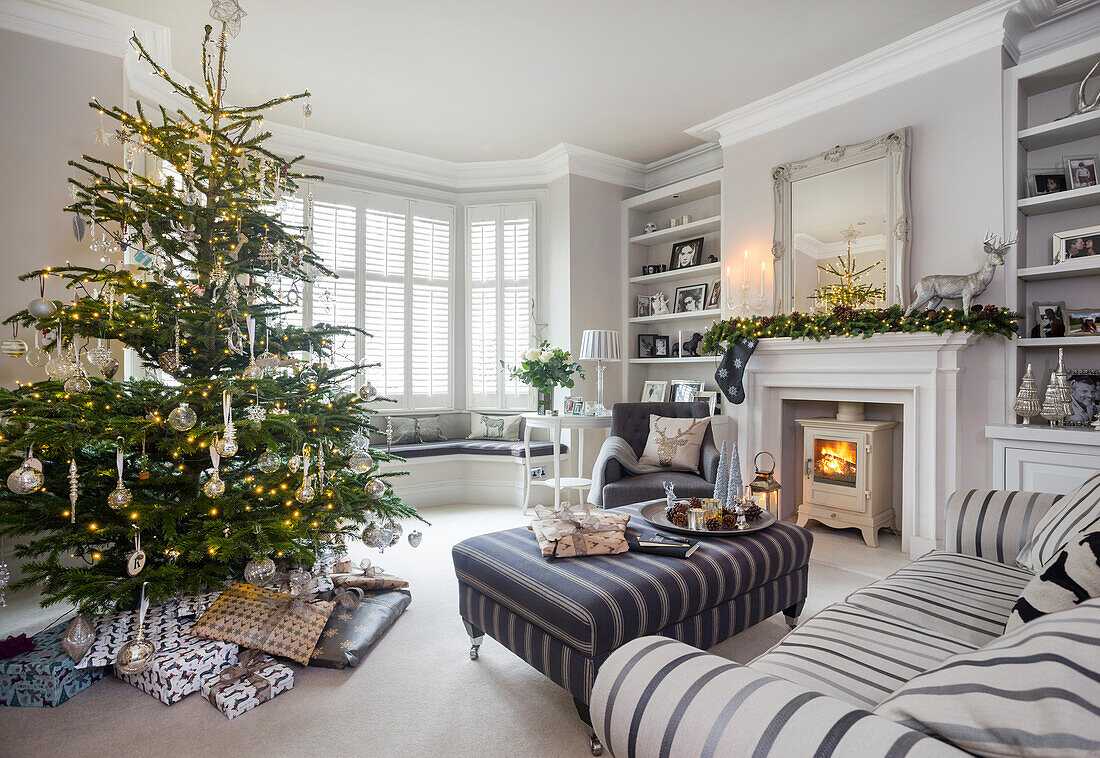 Christmas presents under tree with lit woodburner in London home UK