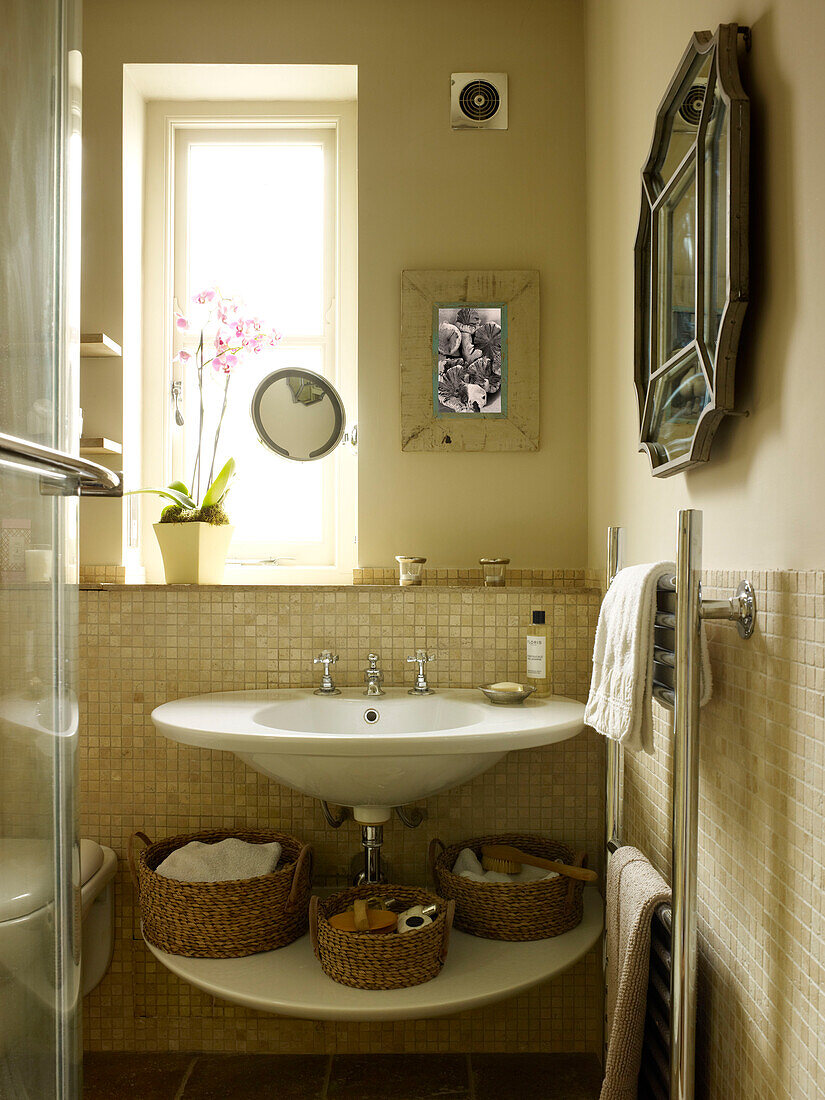 Basket storage under wash basin at window in bathroom of Kensington home London England UK
