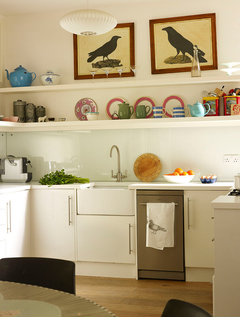 Artwork and open shelving above sink with dishwasher in kitchen of London home England UK