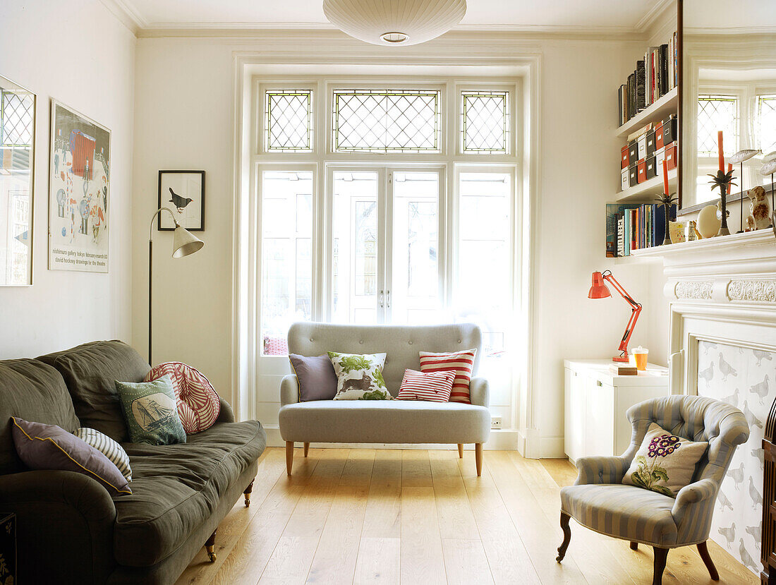 Sofas with cushions and sunlit French doors in living room of London home England UK